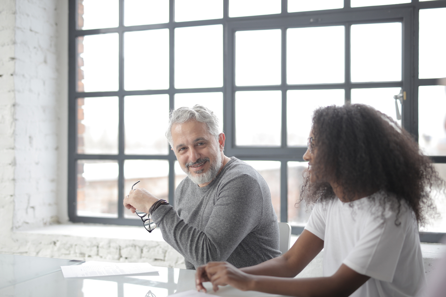 Cheerful senior gray haired mentor supporting young black colleague in office